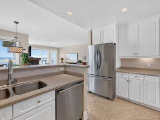 Experience breathtaking ocean views from this stunning kitchen, featuring a spacious double sink, stainless steel appliances including a French door refrigerator, and ample white cabinetry.