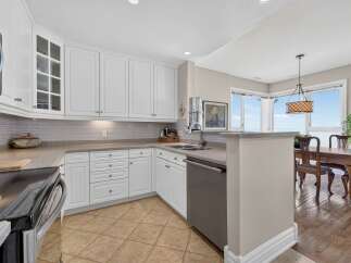 Experience breathtaking ocean views from this stunning kitchen, featuring elegant white cabinetry and a sleek, modern backsplash.