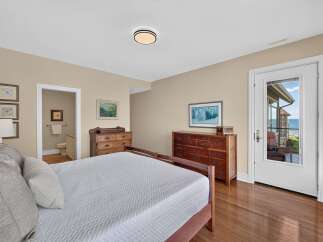 Experience coastal living in this charming bedroom featuring a comfortable bed, ample storage with two wooden dressers, and a private ensuite bathroom.