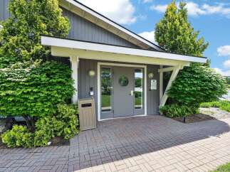 Discover the inviting entrance to this property, featuring a modern gray double door with a circular window, flanked by lush green landscaping.