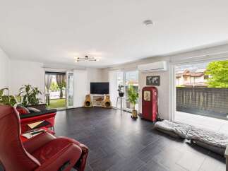 This spacious living area features a modern aesthetic with sleek dark tile flooring and a comfortable red leather recliner.