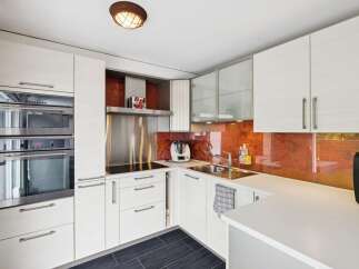 This modern kitchen features sleek white cabinetry and a striking orange backsplash, creating a vibrant and stylish cooking space.