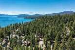 Experience the ultimate lakeside living with this stunning aerial view of a property nestled amidst a dense pine forest, offering breathtaking vistas of a crystal-clear blue lake.