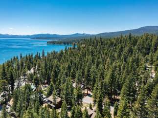 Experience the ultimate lakeside living with this stunning aerial view of a property nestled amidst a dense pine forest, offering breathtaking vistas of a crystal-clear blue lake.