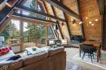 Experience rustic charm in this A-frame cabin living room, featuring a stunning wood-paneled interior with exposed beams and a wall of windows offering breathtaking mountain views.