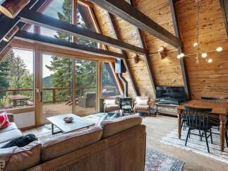 Experience rustic charm in this A-frame cabin living room, featuring a stunning wood-paneled interior with exposed beams and a wall of windows offering breathtaking mountain views.
