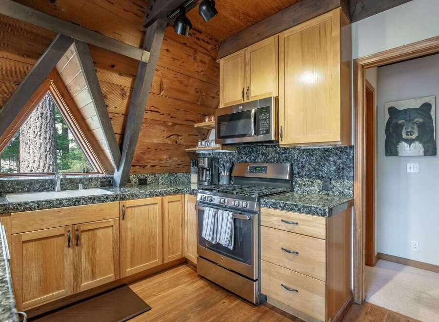 Experience rustic charm in this mountain kitchen, featuring warm wood cabinetry and a striking triangular window with forest views.
