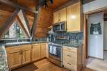 Experience rustic charm in this mountain kitchen, featuring warm wood cabinetry and a striking triangular window with forest views.