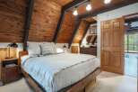 Experience rustic charm in this cozy bedroom featuring a wooden plank A-frame ceiling with exposed beams and a comfortable bed adorned with plush linens.