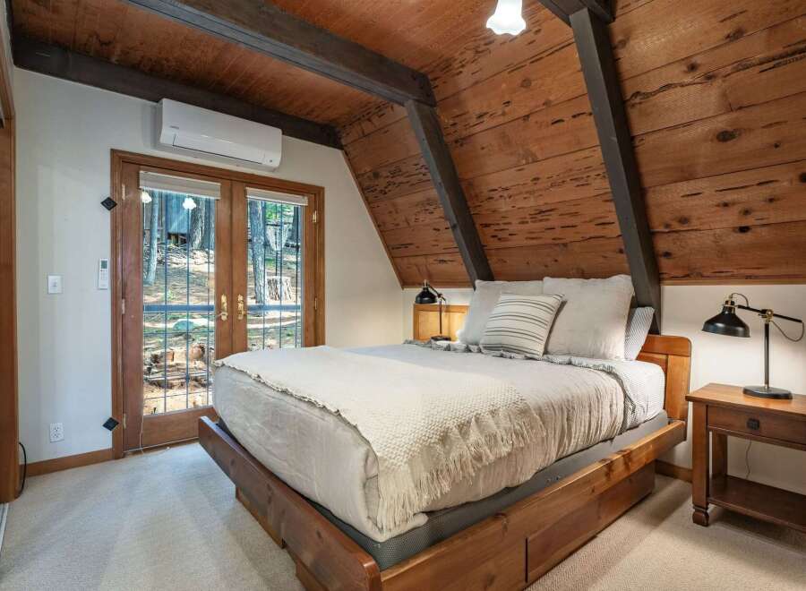 Experience rustic charm in this cozy bedroom featuring a wooden A-frame ceiling and exposed beams.