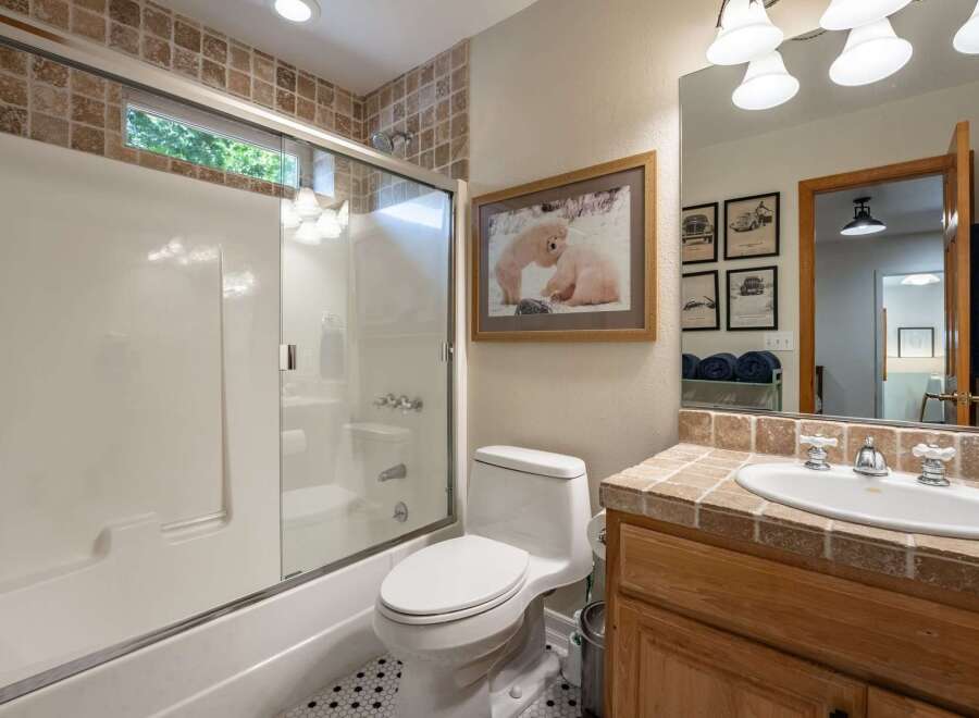 This charming bathroom features a spacious bathtub/shower combo with a sliding glass door and elegant tile accents.