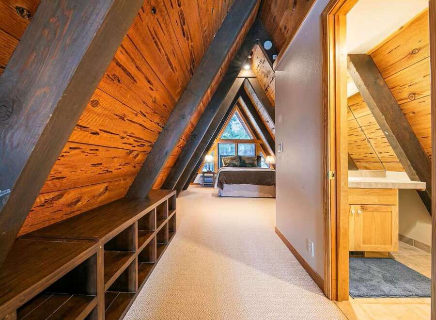 Experience unique A-frame living with this charming bedroom featuring rustic wooden beams and a cozy lofted feel.
