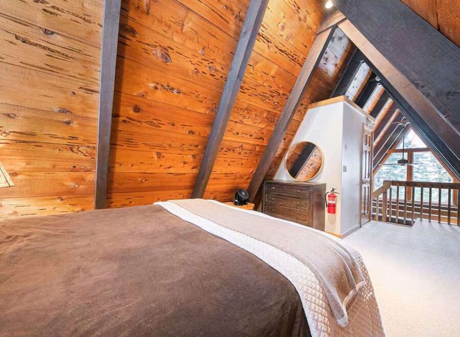 Experience rustic charm in this A-frame bedroom, featuring warm wood-paneled walls and exposed beams that create a cozy, cabin-like atmosphere.