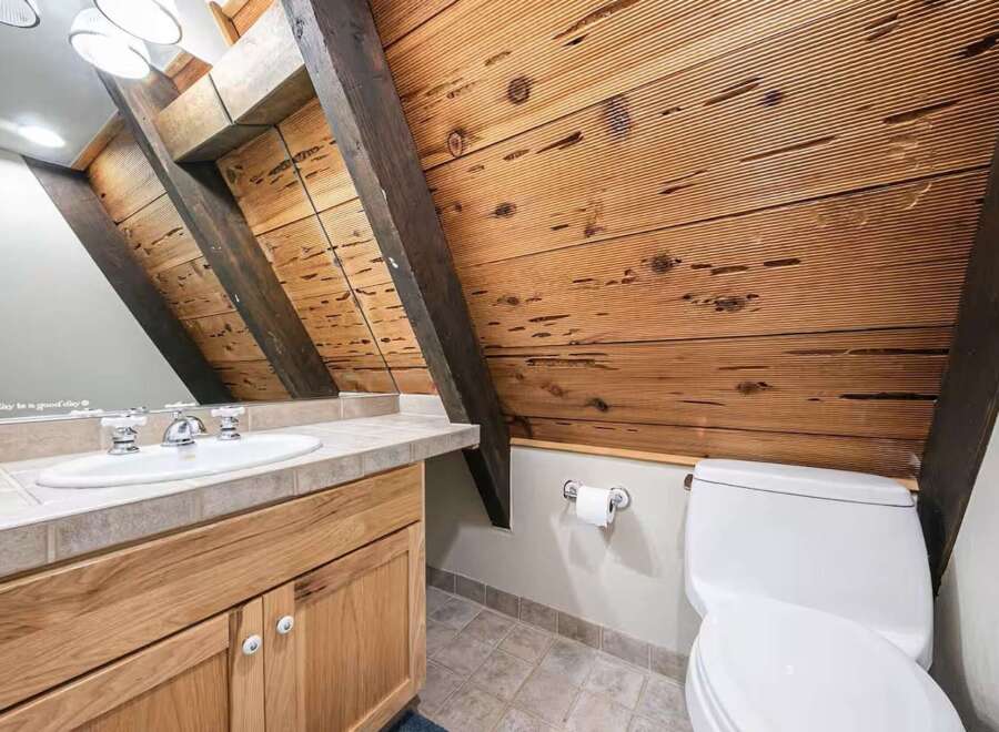 Experience rustic charm in this unique bathroom featuring exposed wooden beams and a slatted wood ceiling.