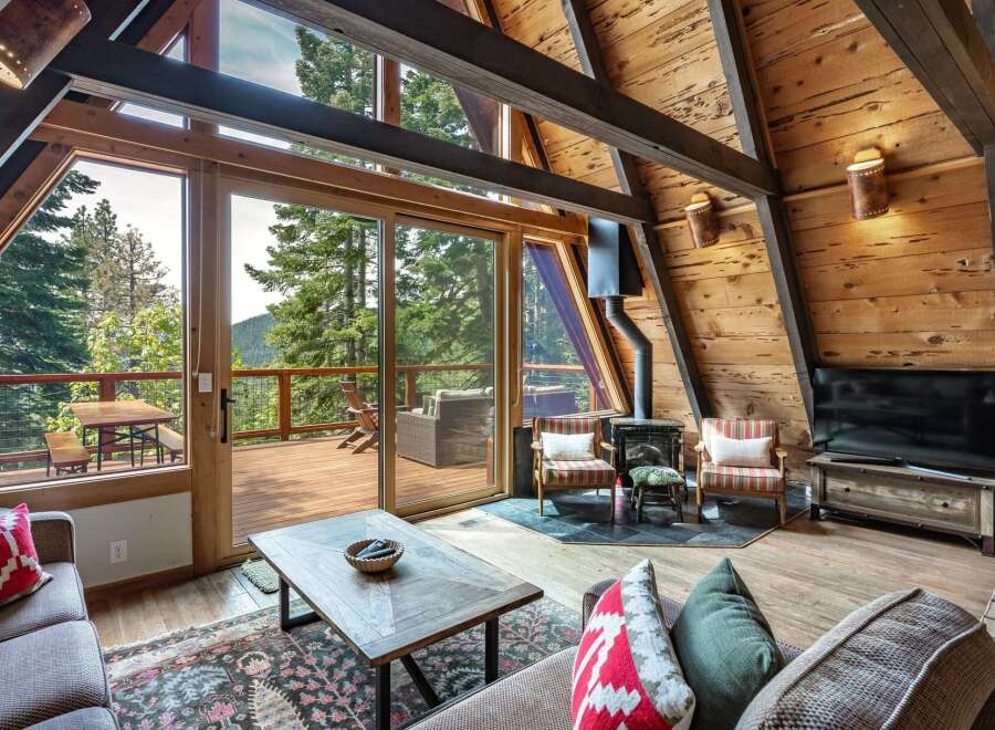 Experience breathtaking mountain views from this stunning A-frame cabin living room, featuring a cozy fireplace and expansive windows that seamlessly blend indoor and outdoor living.
