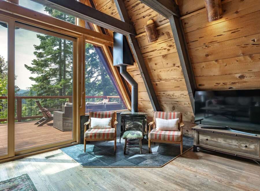 Experience rustic charm in this A-frame cabin living room, featuring a cozy fireplace and stunning mountain views through expansive glass doors.