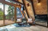 Experience rustic charm in this A-frame cabin living room, featuring a cozy fireplace and stunning mountain views through expansive glass doors.