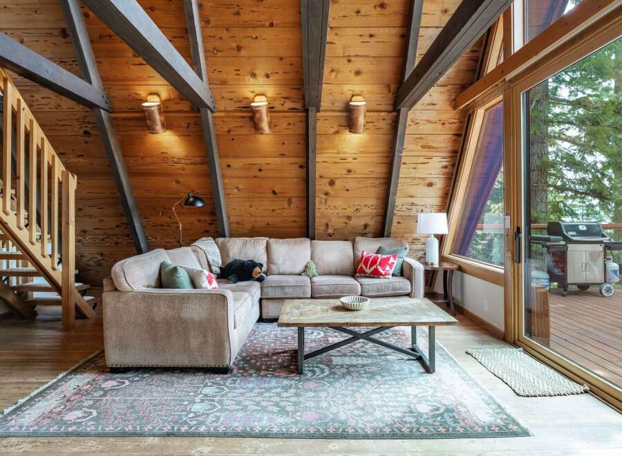 Experience rustic charm in this A-frame living room, featuring exposed wooden beams and a cozy sectional sofa perfect for gathering.