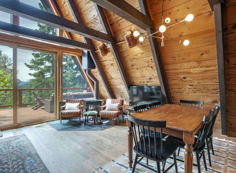 Experience rustic charm in this A-frame cabin living area, featuring a cozy fireplace and a dining set perfect for intimate gatherings.