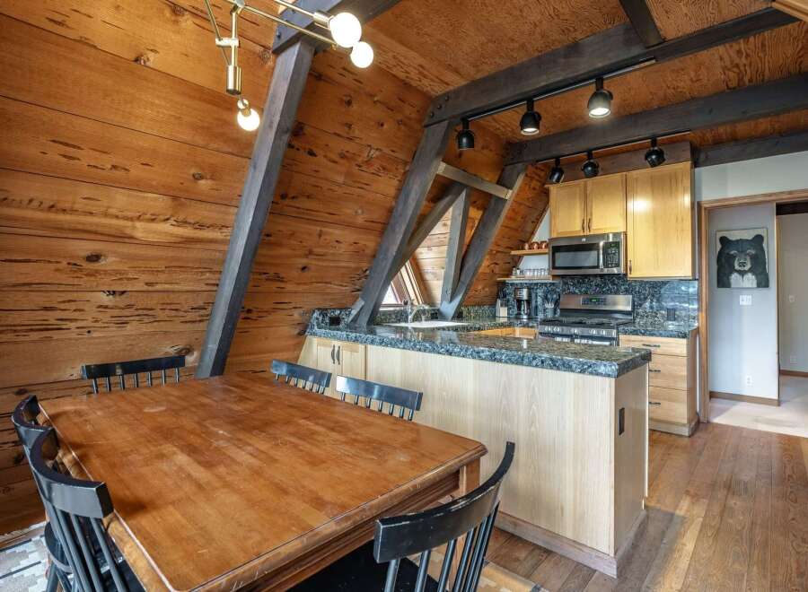 Experience rustic charm in this A-frame kitchen and dining area, featuring warm wood paneling and exposed beams.