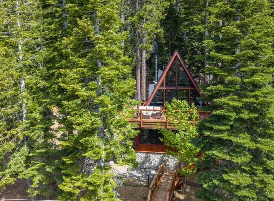 Nestled amidst lush green trees, this A-frame cabin offers a unique architectural design with expansive glass windows that bring the outdoors in.