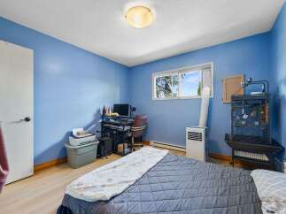 This cozy bedroom features a comfortable bed, a functional workspace with a computer and printer, and a large window offering natural light.