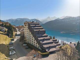 Experience breathtaking panoramic views from this unique, tiered apartment building nestled against a stunning mountain backdrop and a serene lake.