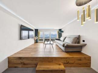 Experience breathtaking mountain views from this modern living room, featuring a unique raised wooden platform with integrated storage.