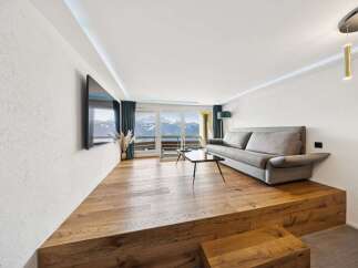Experience breathtaking mountain views from this modern living room, featuring a raised wooden platform and a sleek sofa.