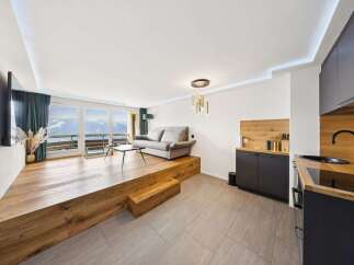 Experience modern living in this stunning apartment featuring a raised wooden living area with a comfortable sofa and breathtaking mountain views through expansive windows.