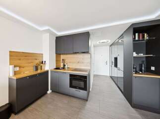 Discover modern living in this sleek studio apartment, featuring a compact yet fully equipped kitchenette with dark cabinetry and a wooden backsplash.