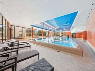 Experience ultimate relaxation in this indoor swimming pool area, featuring a stunning blue ceiling that mimics the sky and ample lounge chairs for sunbathing.