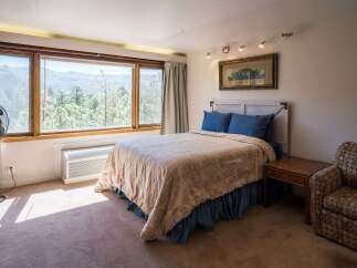 Experience breathtaking mountain views from this charming bedroom, featuring a comfortable queen-size bed adorned with blue patterned pillows and a floral comforter.