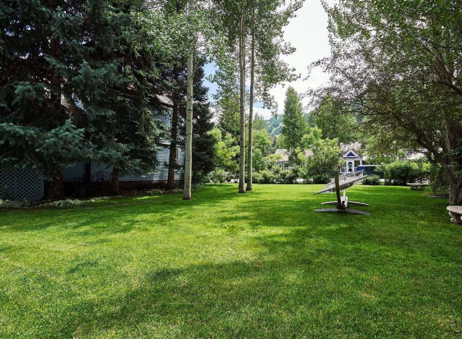 This expansive backyard offers a serene escape with lush green grass and mature trees providing ample shade.
