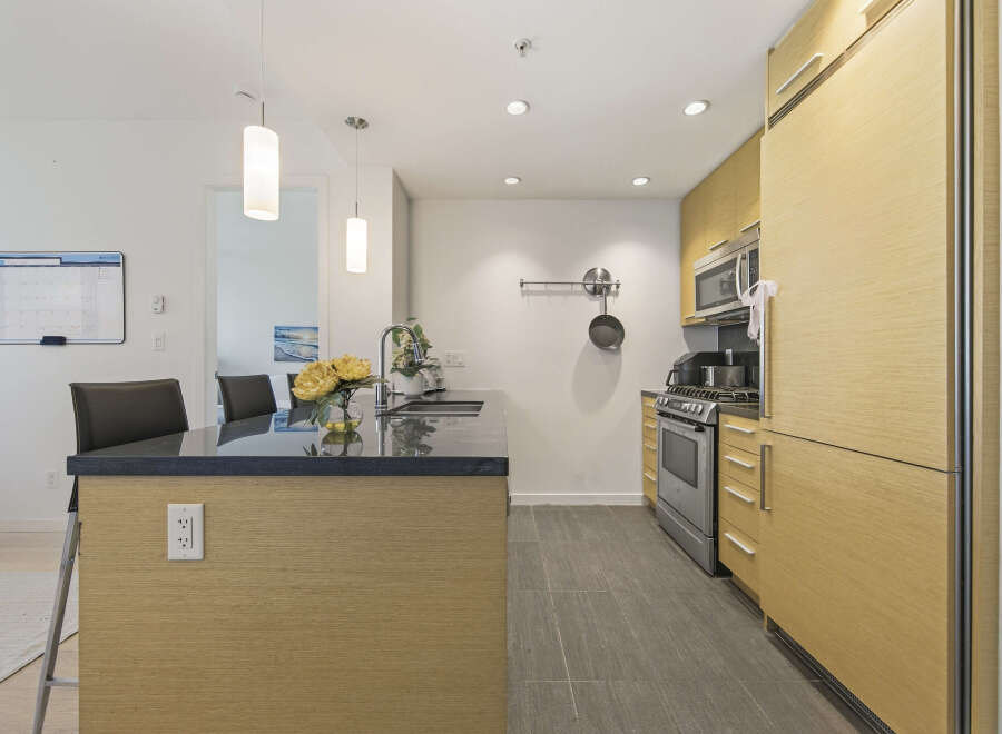 This modern kitchen boasts sleek, light wood cabinetry and a spacious island with a dark granite countertop.