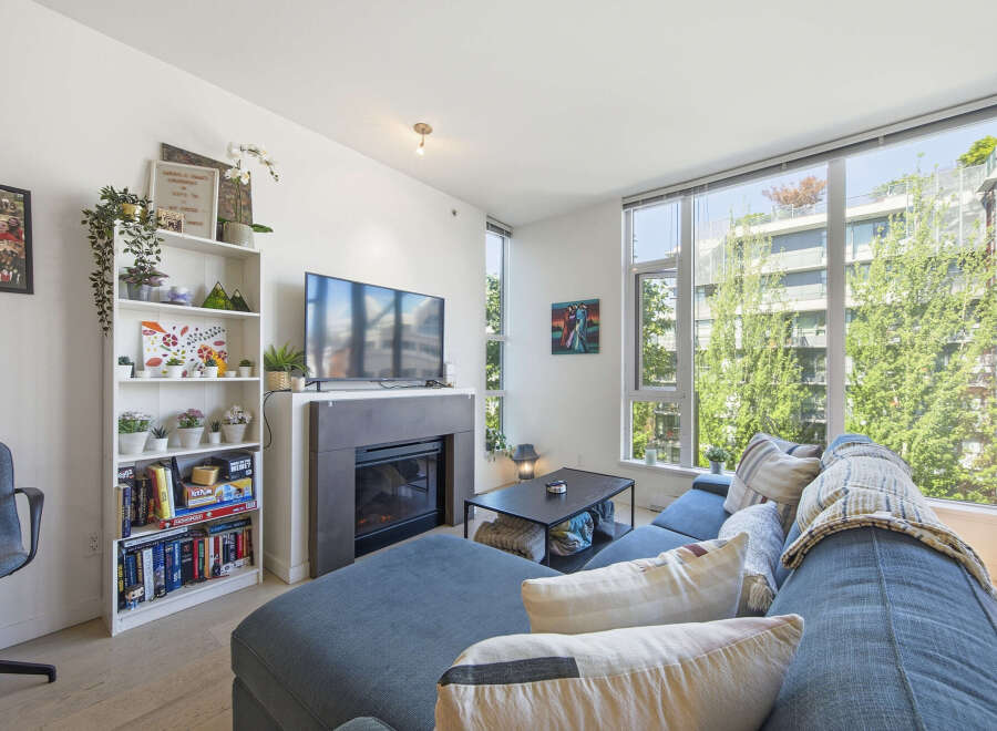 Bright and airy living room featuring a large sectional sofa, a modern fireplace, and expansive windows offering lush green views.