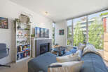 Bright and airy living room featuring a large sectional sofa, a modern fireplace, and expansive windows offering lush green views.
