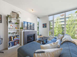 Bright and airy living room featuring a large sectional sofa, a modern fireplace, and expansive windows offering lush green views.