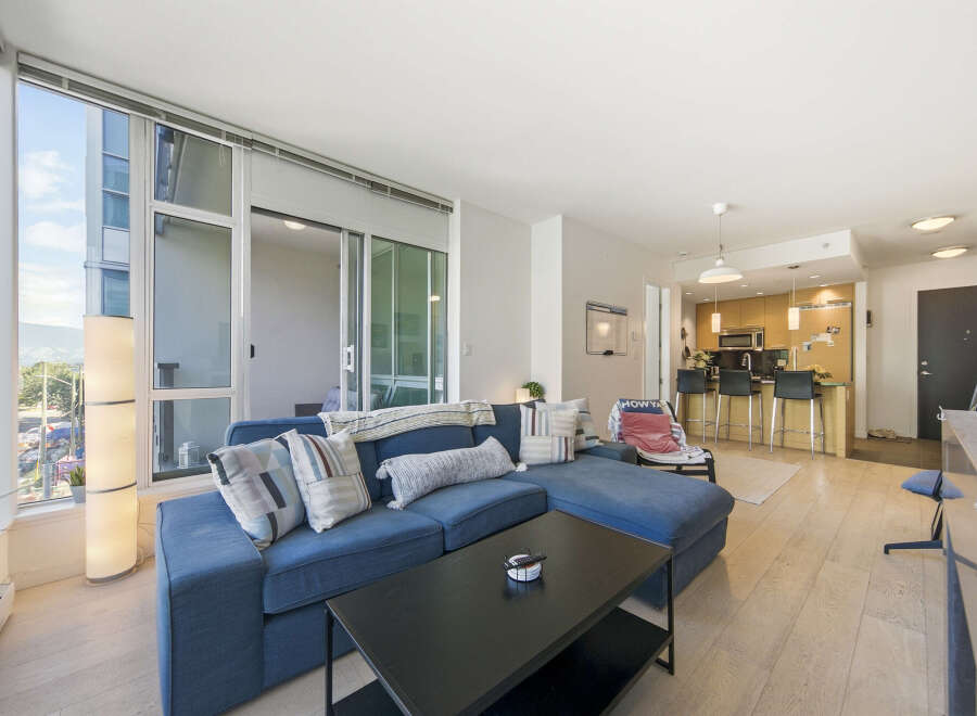 Experience modern urban living in this stunning condo featuring a spacious open-concept living area with a large sectional sofa and a sleek black coffee table.