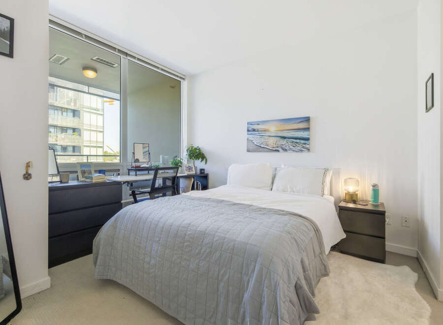 Experience modern urban living in this stylish bedroom, featuring a comfortable bed adorned with a plush grey quilt.