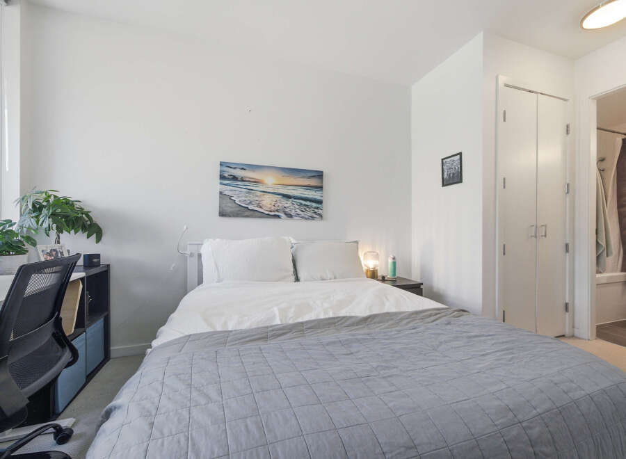 Discover comfort and style in this inviting bedroom, featuring a plush queen-size bed adorned with crisp white linens and a cozy grey quilt.
