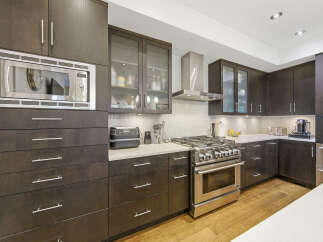 Experience culinary excellence in this modern kitchen, featuring sleek dark wood cabinetry and a professional-grade stainless steel gas range.
