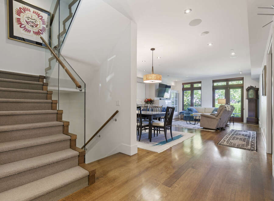 Step into this stunning modern home featuring a sleek staircase with glass railings and a warm, inviting open-concept living area.