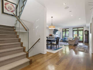 Step into this stunning modern home featuring a sleek staircase with glass railings and a warm, inviting open-concept living area.