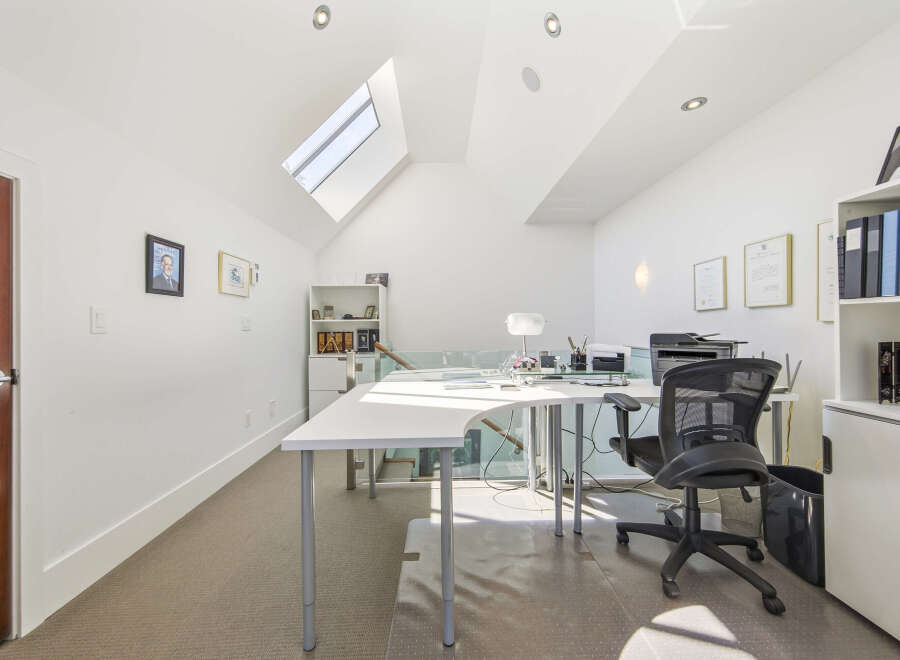 This bright and airy home office features a modern white L-shaped desk with ample workspace, complemented by a comfortable black ergonomic chair.