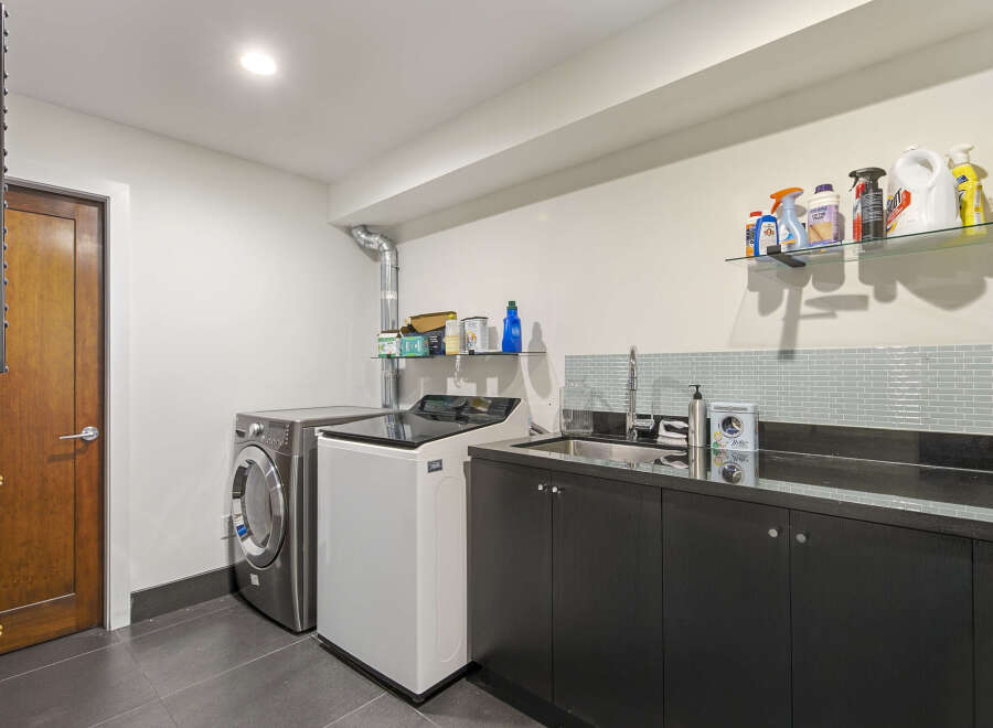 This laundry room features a sleek, modern design with a stainless steel washing machine and a white top-load washer.