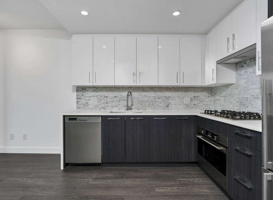 This modern kitchen features sleek white upper cabinets and dark wood lower cabinets, complemented by a stylish marble tile backsplash.