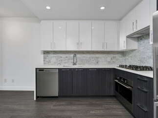 This modern kitchen features sleek white upper cabinets and dark wood lower cabinets, complemented by a stylish marble tile backsplash.