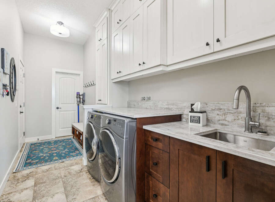 This spacious laundry room boasts ample storage with floor-to-ceiling white cabinets and rich wood cabinetry below the marble countertops.