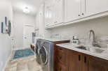 This spacious laundry room boasts ample storage with floor-to-ceiling white cabinets and rich wood cabinetry below the marble countertops.